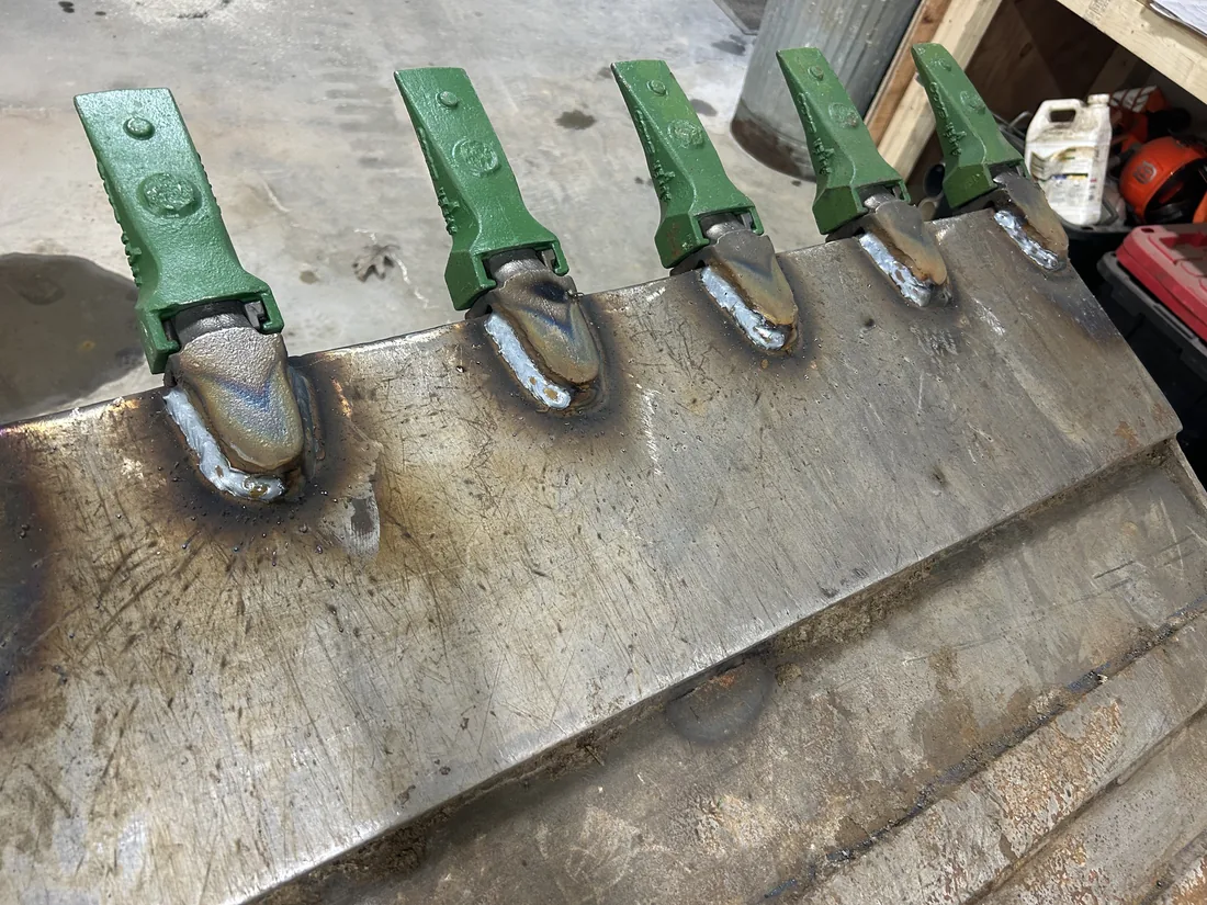 New tooth adapters welded onto the cutting edge of an excavator bucket during a rebuild