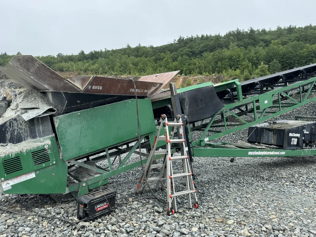 Tracked screening plant in a yard with a ladder set against the hopper for a welding repair