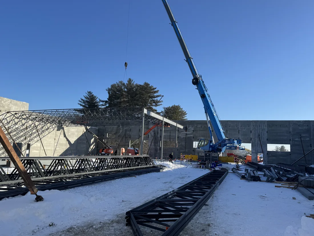 Crane setting bar joists over a concrete shell in winter, joists staged on the slab ready to be flown