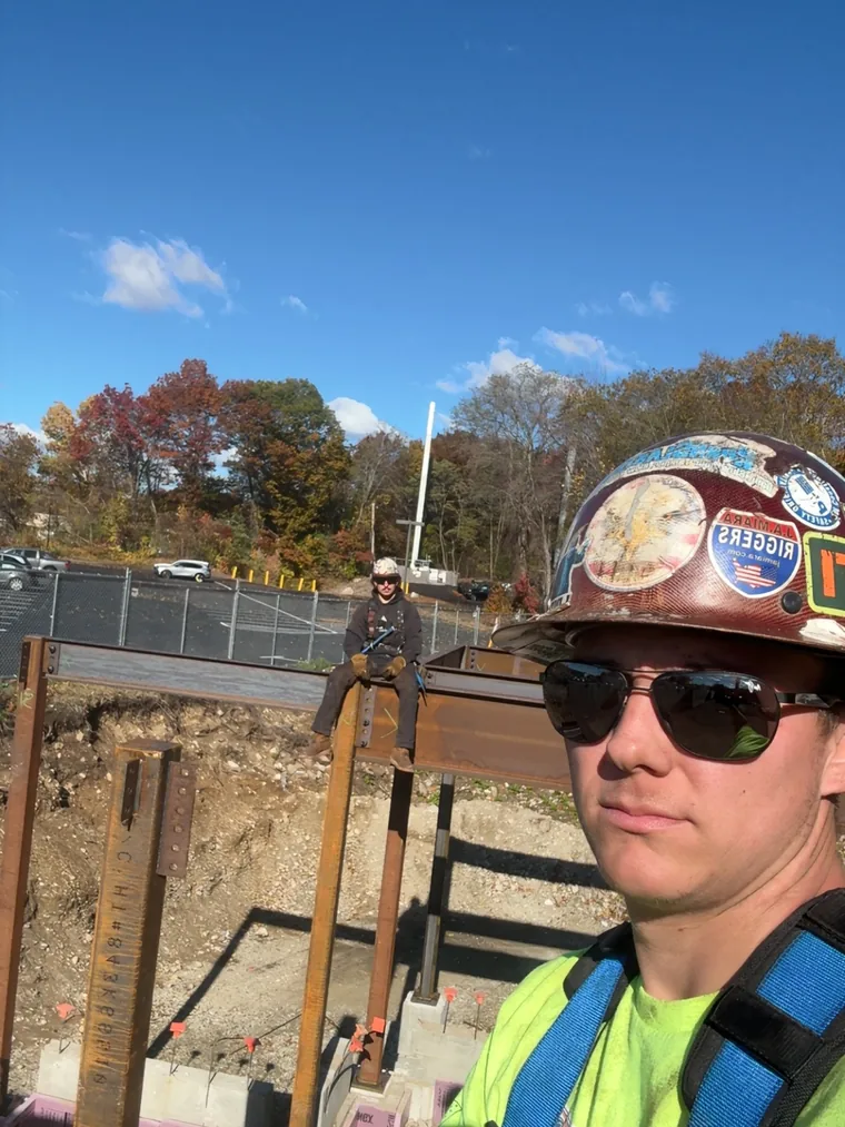 Zachary Oak, owner of 603 Welding and Erection, on a job site in a hard hat, hi-vis and fall protection harness
