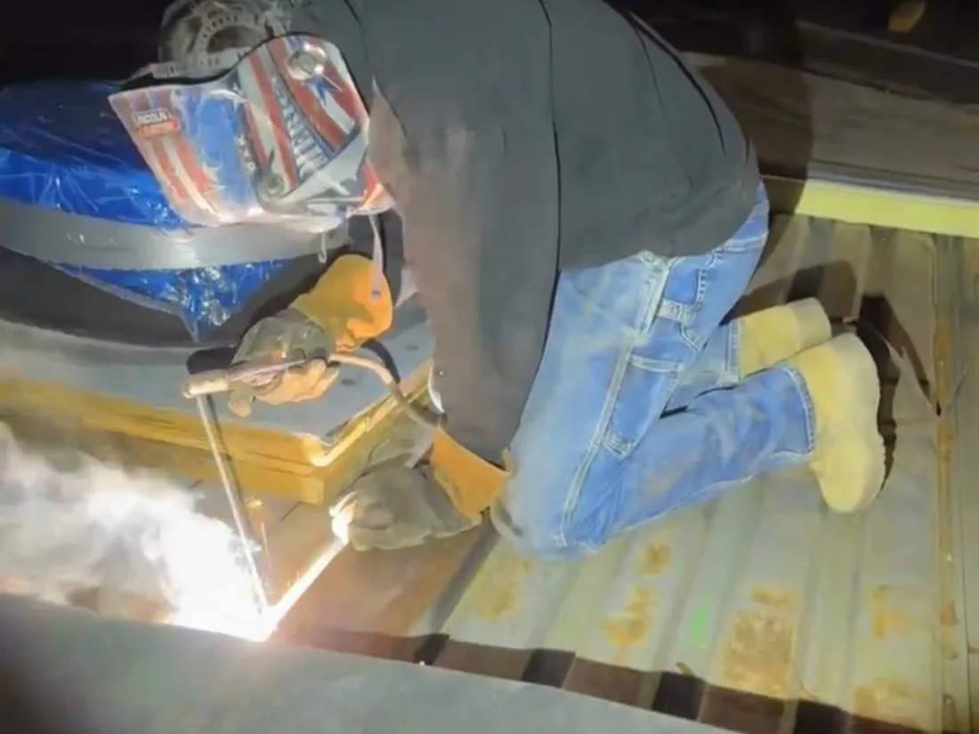 Welder in a hood and gloves running a bead on steel decking, arc lit